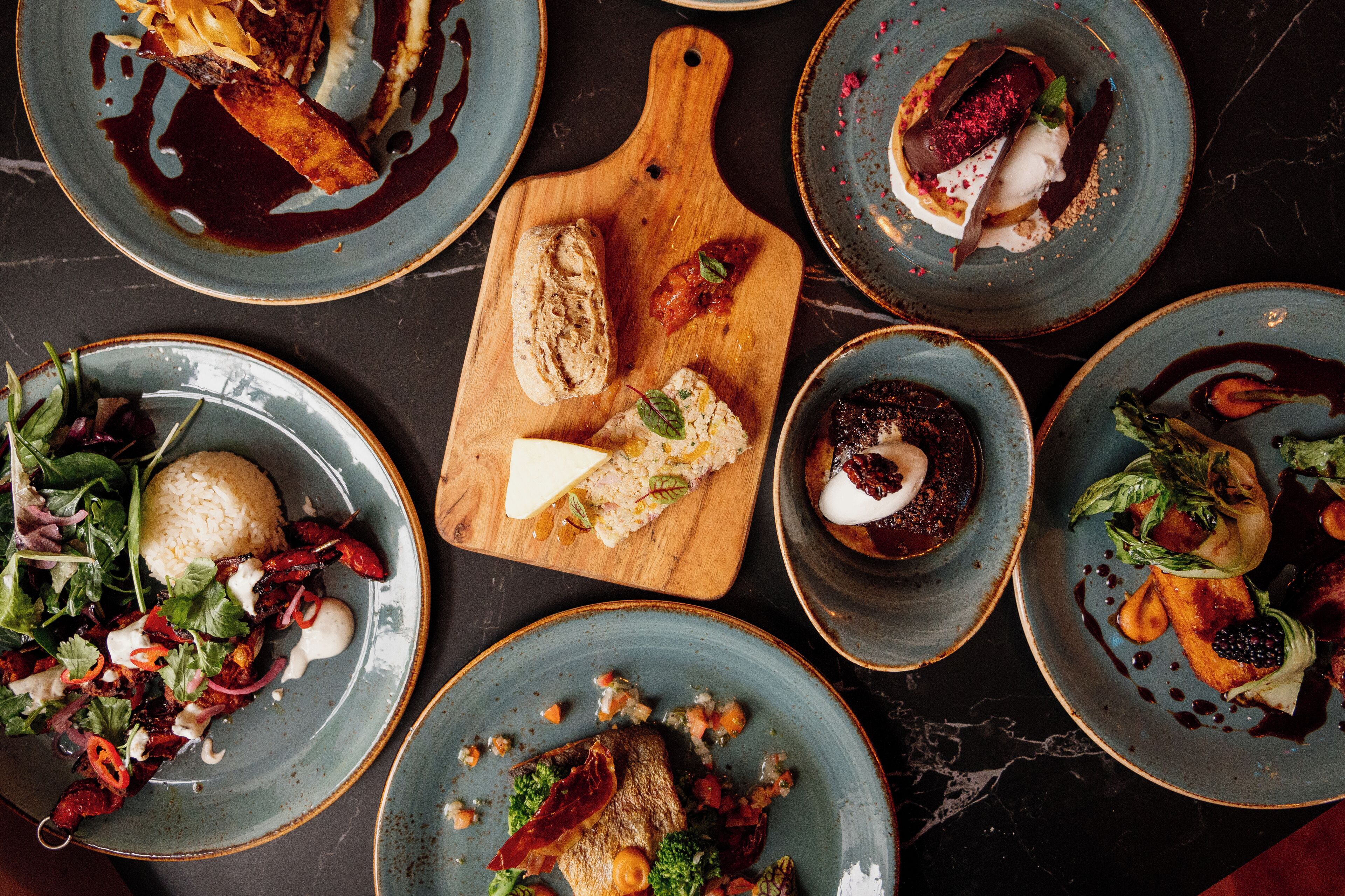 A variety of dishes on plates and a wooden board, suggesting a dining setting.