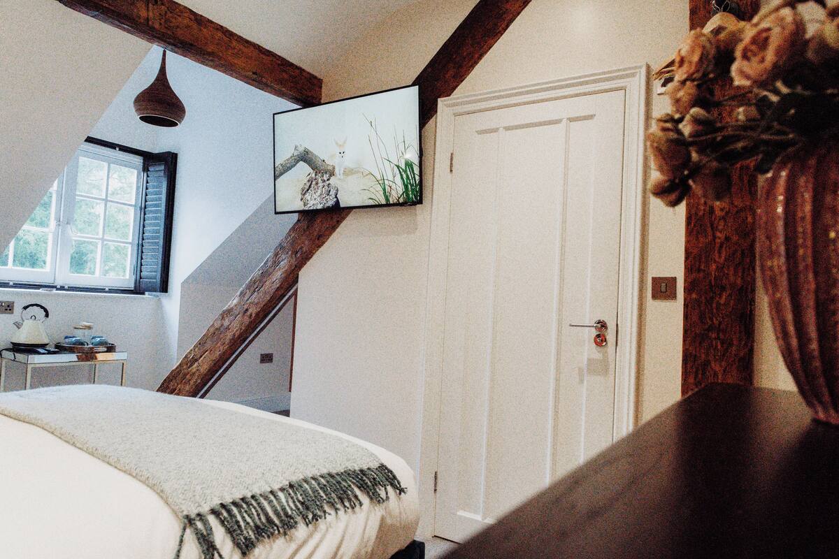 A bedroom with a sloped ceiling, a bed with a white blanket, a wooden headboard, a white door, and a framed picture on the wall.