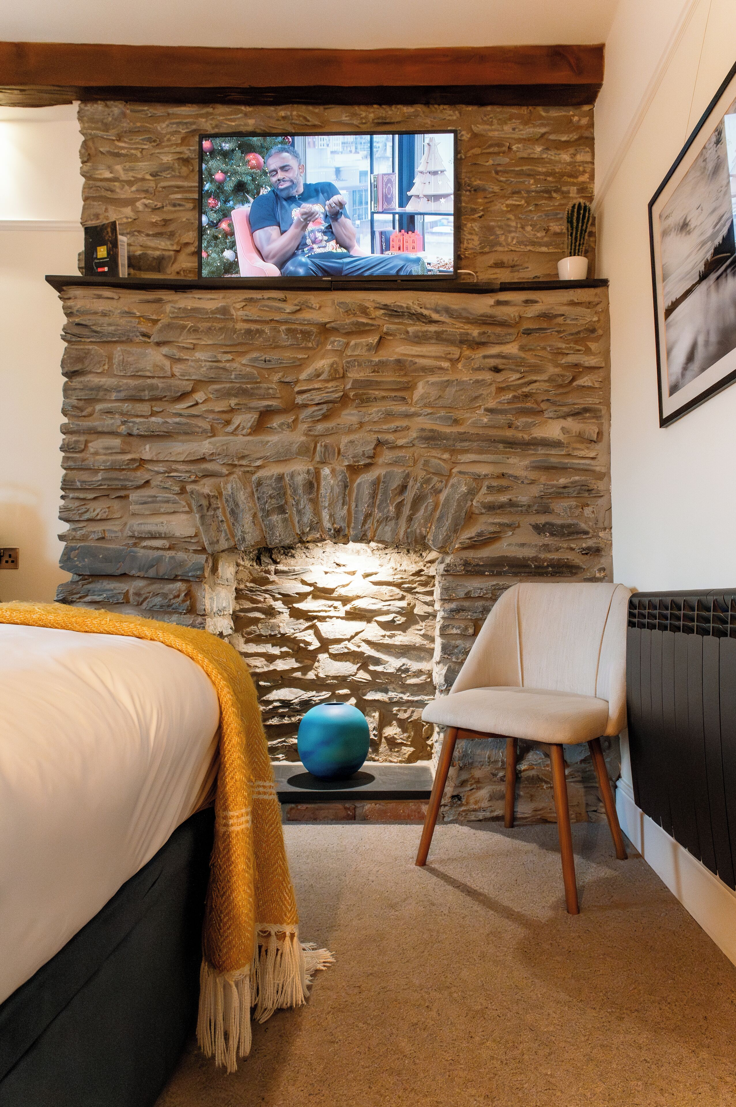 A cozy room with a stone fireplace, a television mounted above it, a bed with a yellow throw, and a chair.