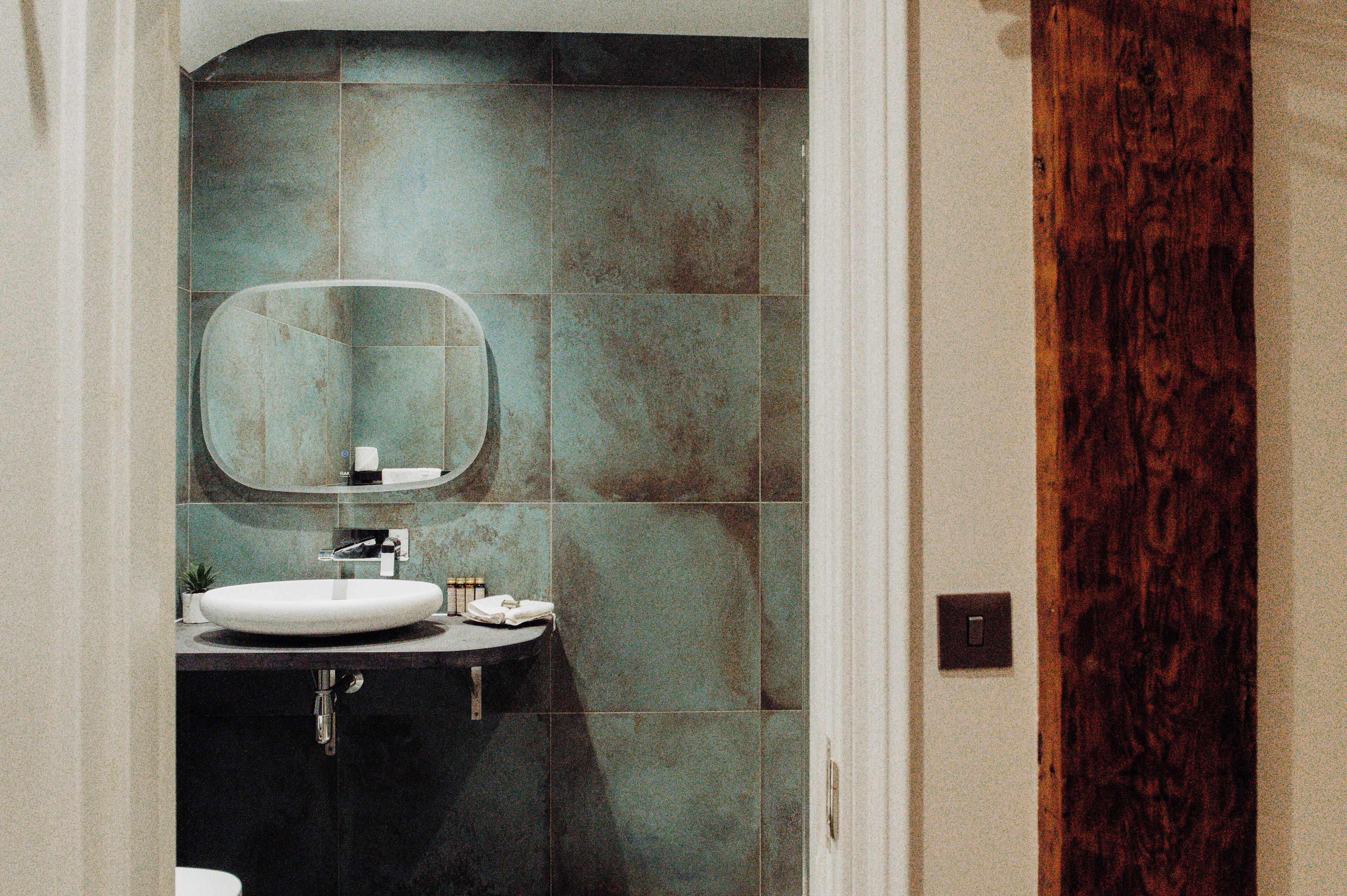 A bathroom with a white sink, a mirror, and a dark tiled wall.