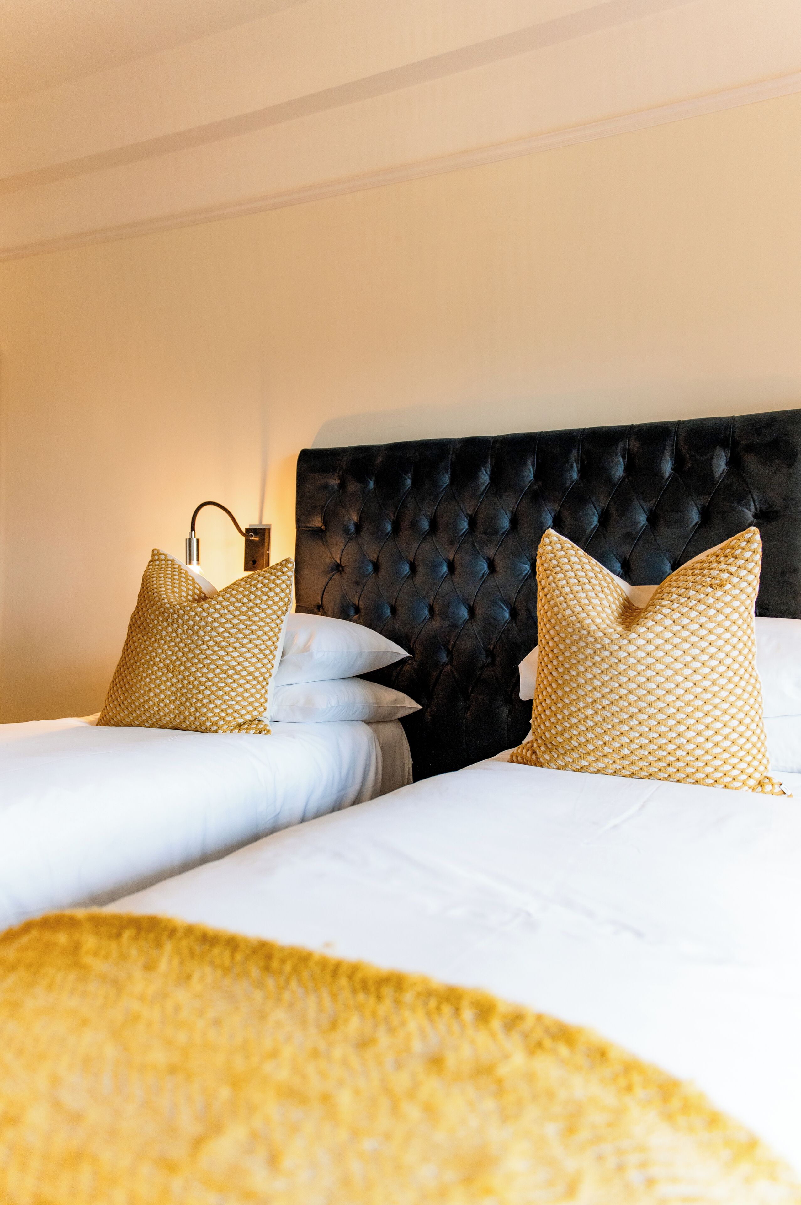 Una cama bien hecha con un cabecero tapizado negro, dos almohadas estampadas y una lámpara de noche.