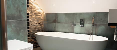 Un baño moderno con una bañera independiente, inodoro y una pared de acento de piedra.