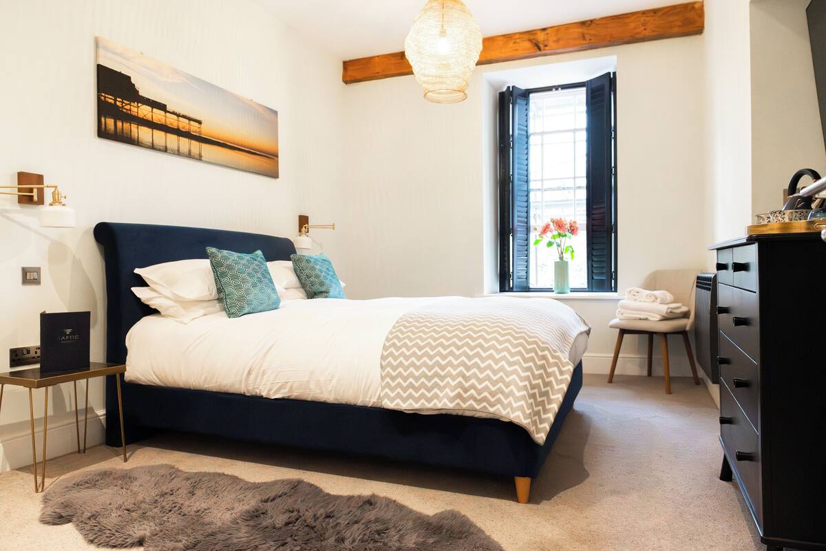 A bedroom with a bed, a dresser, a window with curtains, a painting on the wall, and a rug.