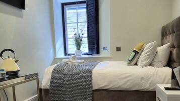 A bedroom with a bed, bedside table, lamp, window, and a small plant.