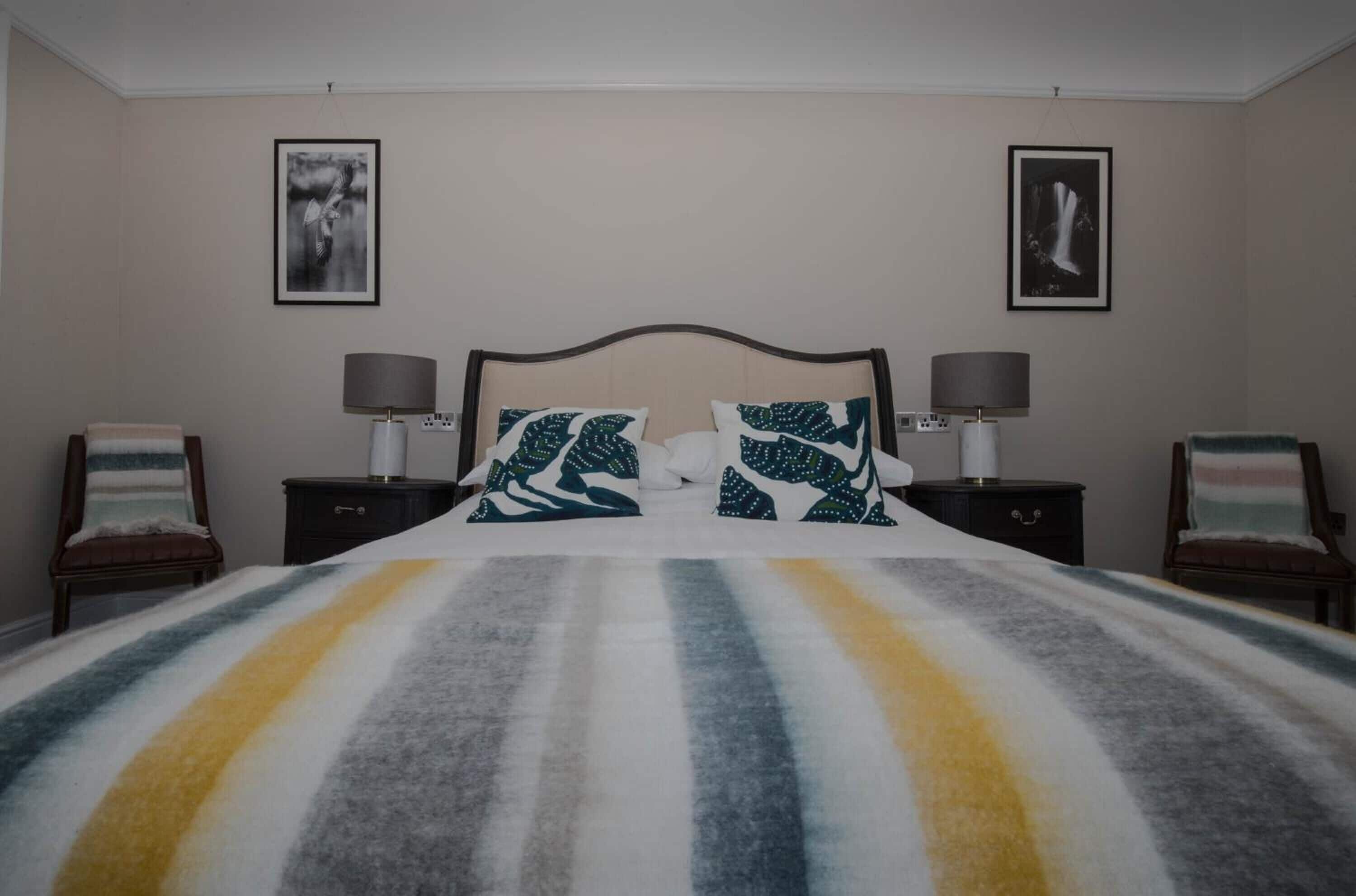 A bedroom with a bed, two nightstands, two chairs, and two wall-mounted lamps.