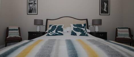 A bedroom with a bed, two nightstands, two chairs, and two wall-mounted lamps.