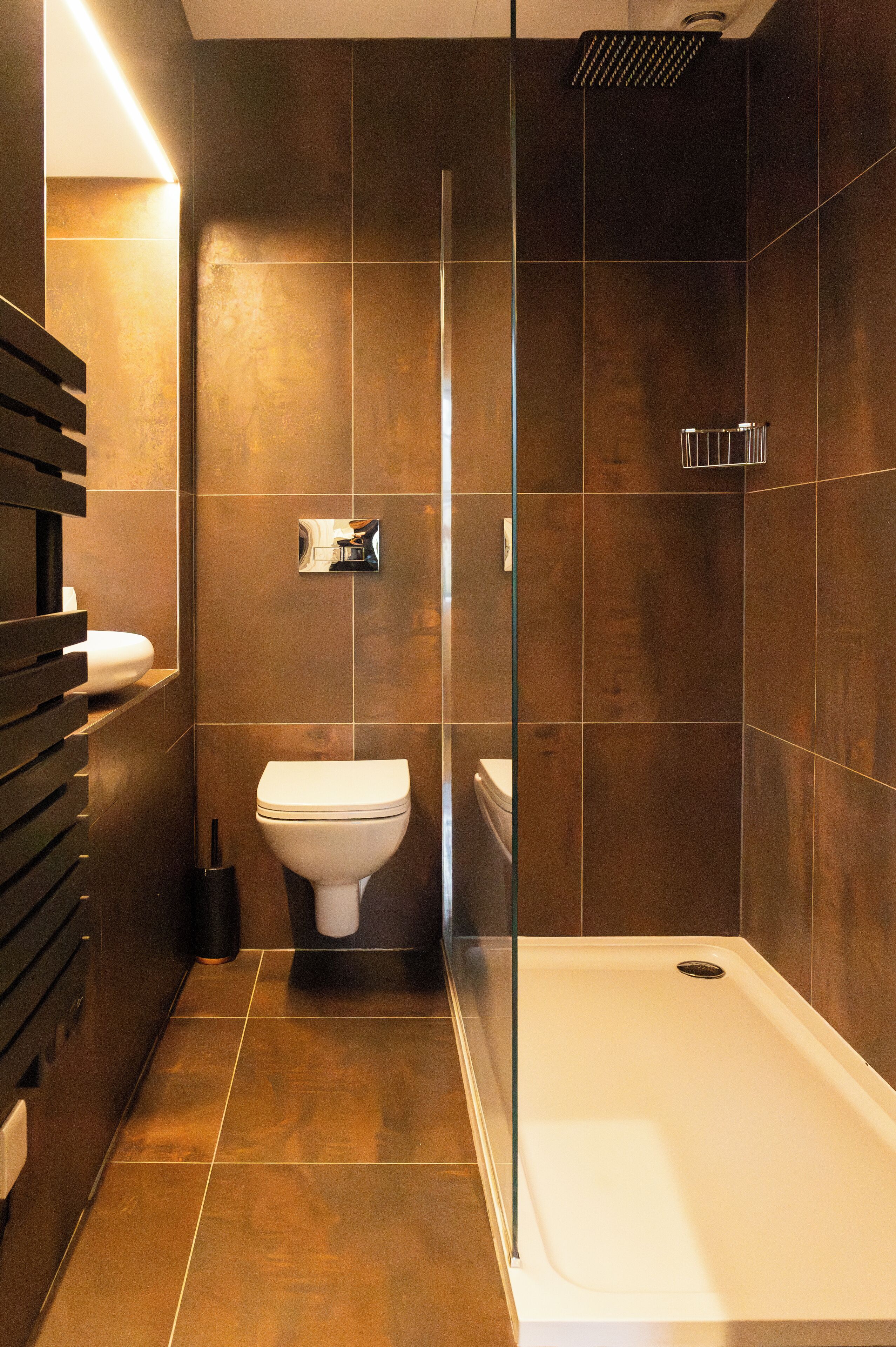Un bagno moderno con cabina doccia in vetro, un WC bianco e una parete rivestita di piastrelle scure.