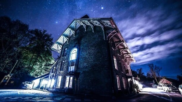 A historic stone building with a large arched window and a sloped roof, illuminated by exterior lighting. - The Hafod Hotel (Aberystwyth)