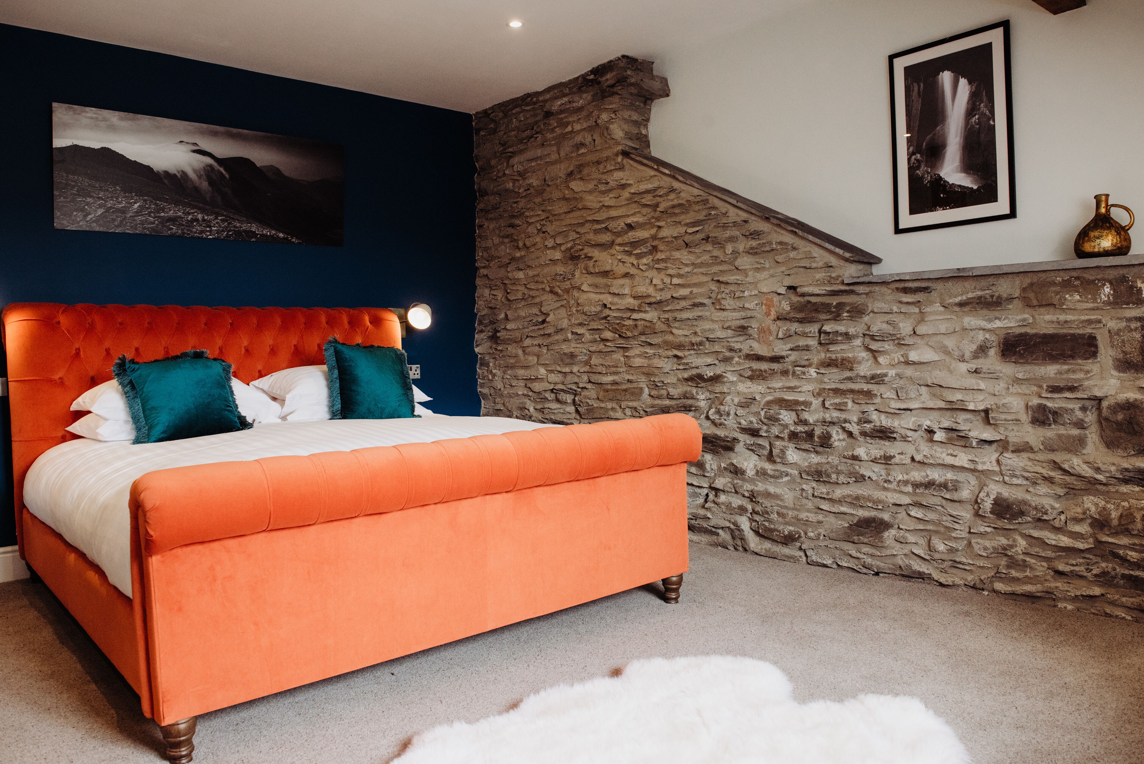 Un dormitorio con una cama grande, una pared de piedra y dos cuadros enmarcados.