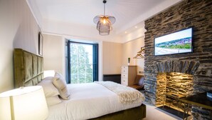 A bedroom with a bed, a lamp, a TV mounted on a stone wall, and a fireplace. - The Hafod Hotel (Aberystwyth)