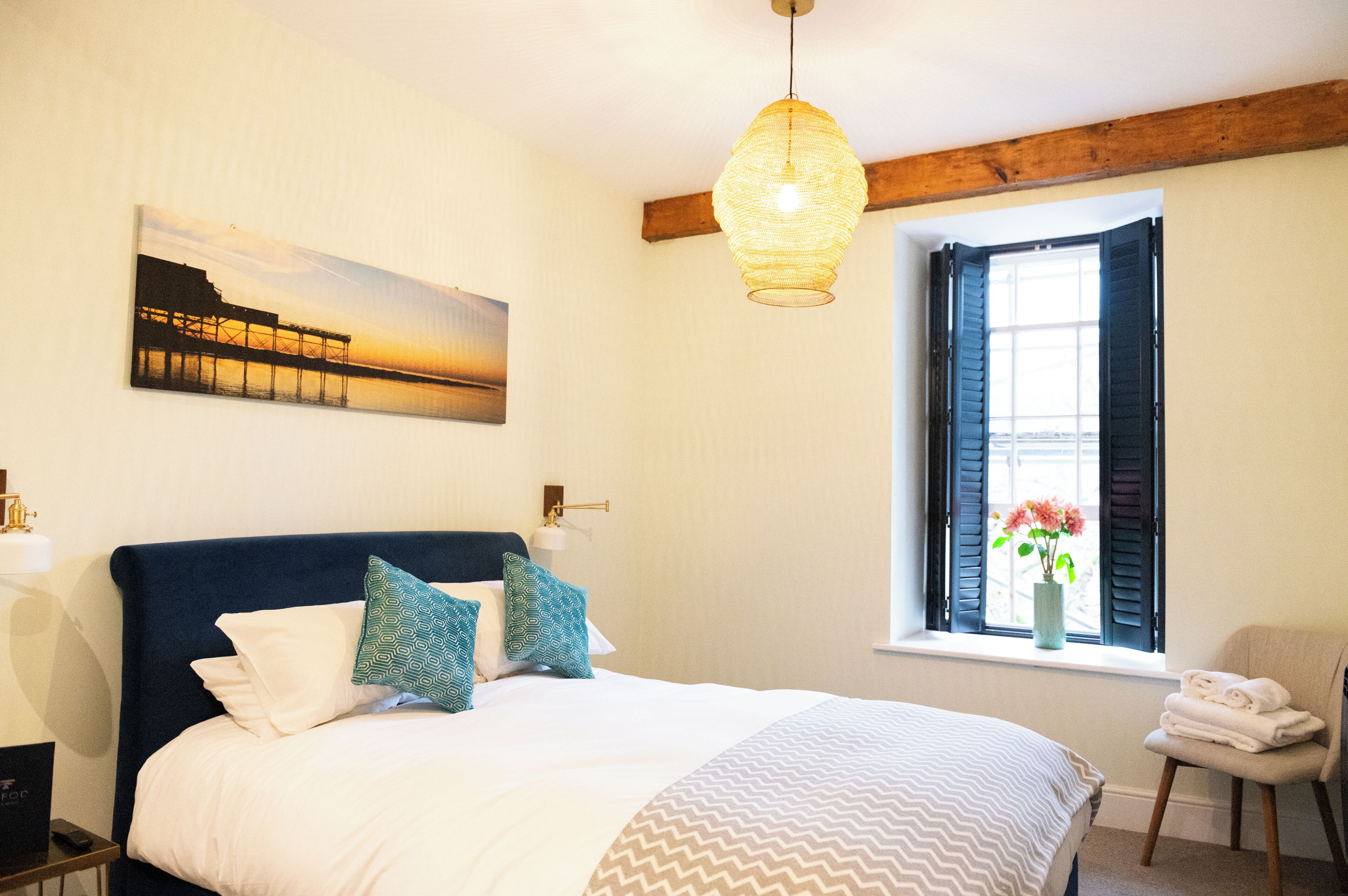 A bedroom with a bed, a window with shutters, a hanging light fixture, and a painting on the wall.