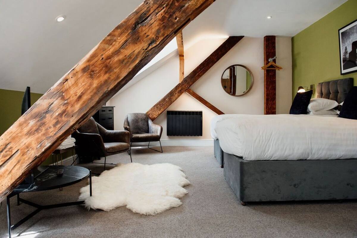 A bedroom with a sloped ceiling, a bed, a chair, a round mirror, and a hanging light fixture.