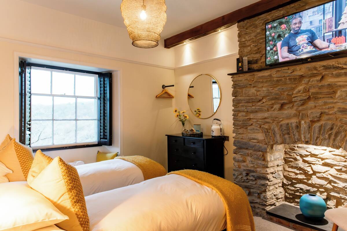 A hotel room with two beds, a stone fireplace, a television, and a window with blinds.