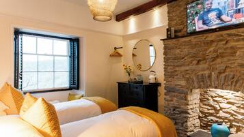 A hotel room with two beds, a stone fireplace, a television, and a window with blinds.
