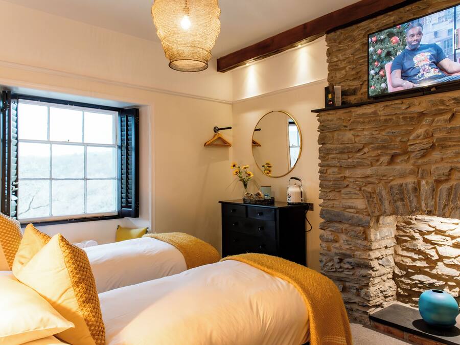 A hotel room with two beds, a stone fireplace, a television, and a window with blinds.
