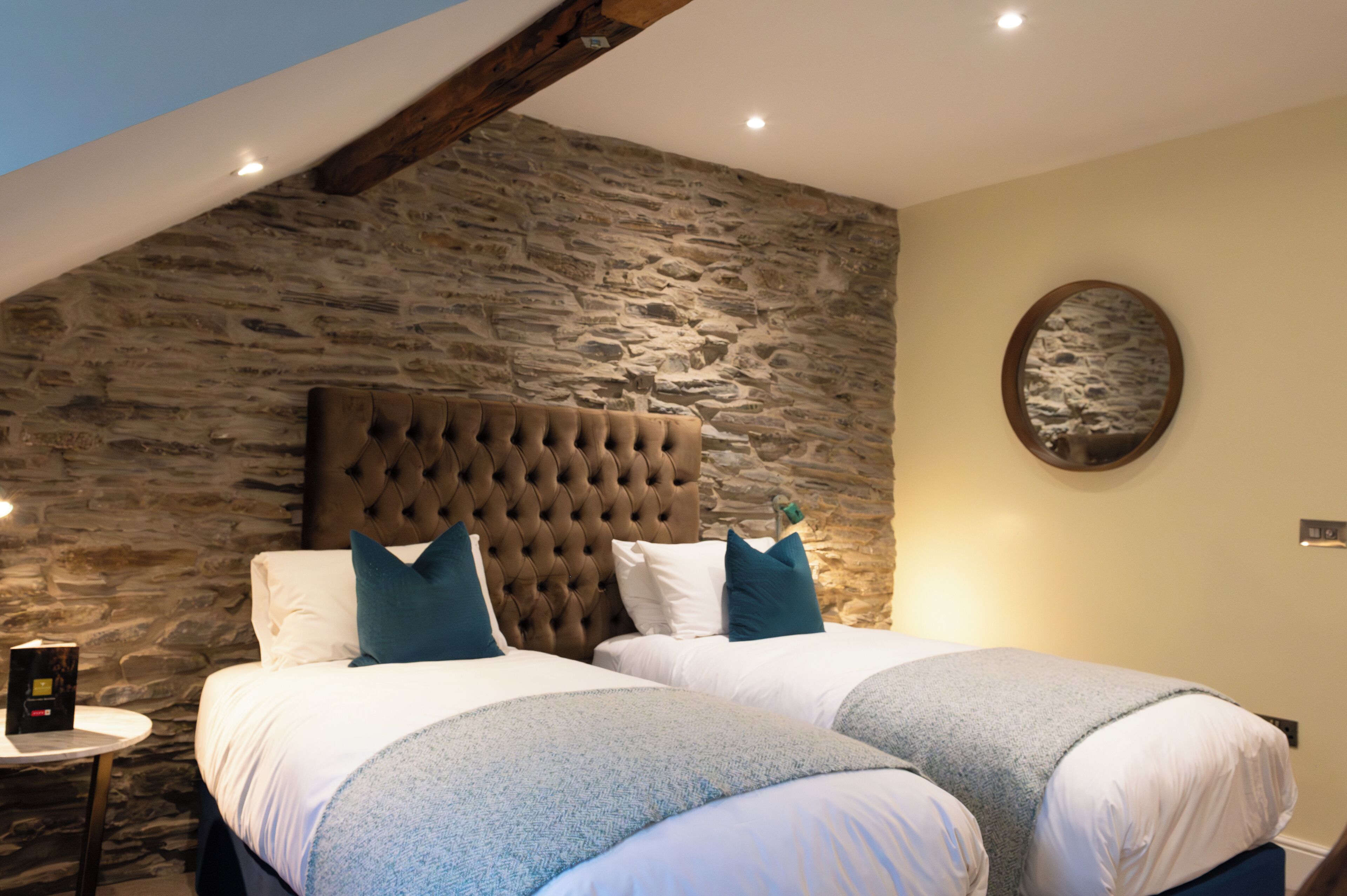 A bedroom with two beds, a stone wall, and a wooden ceiling beam.