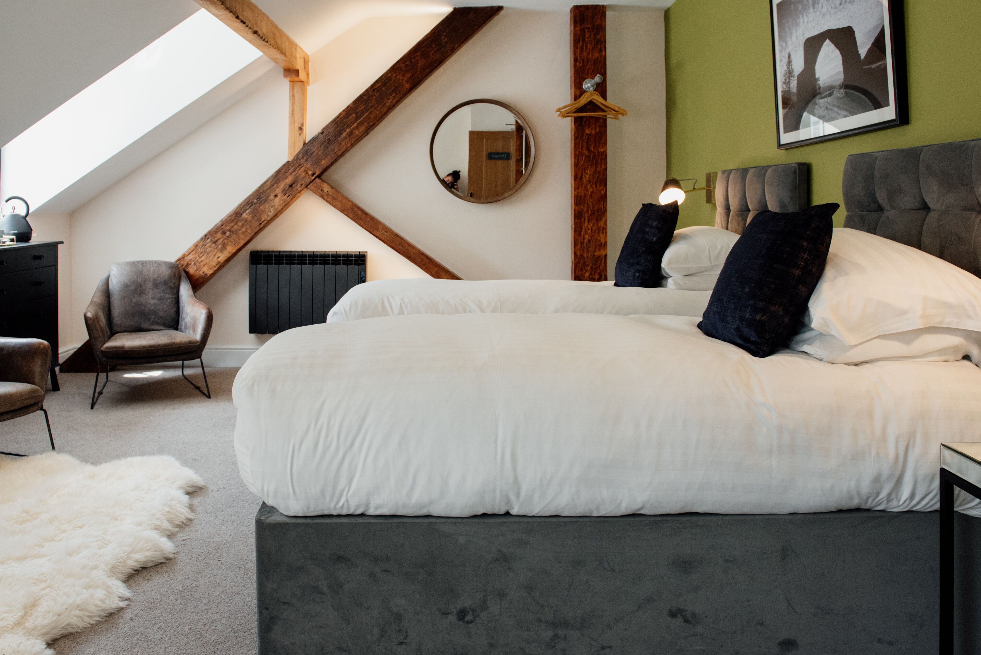 A bedroom with a large bed, a chair, a fur rug, a wooden beam, and a mirror on the wall.