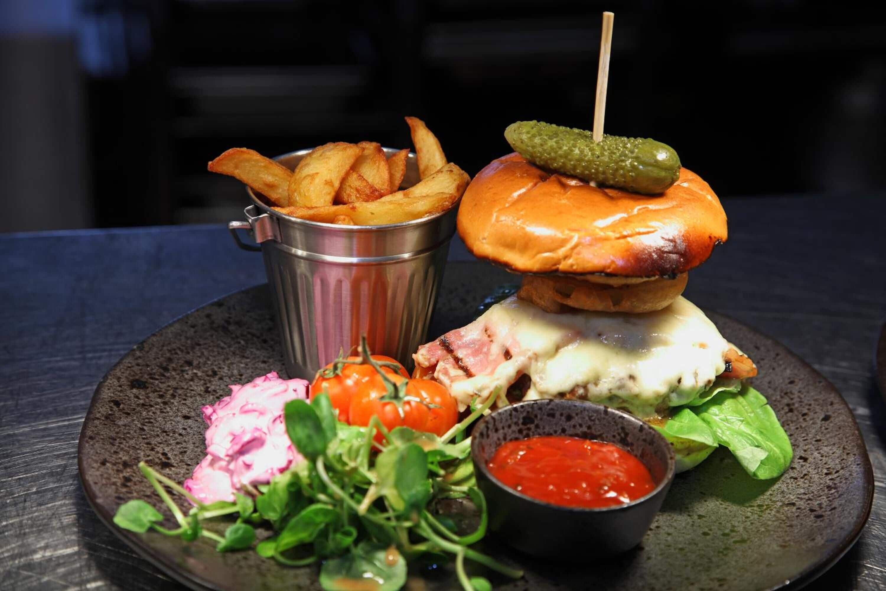 A plate with a burger, fries, cherry tomatoes, lettuce, and two dipping sauces.