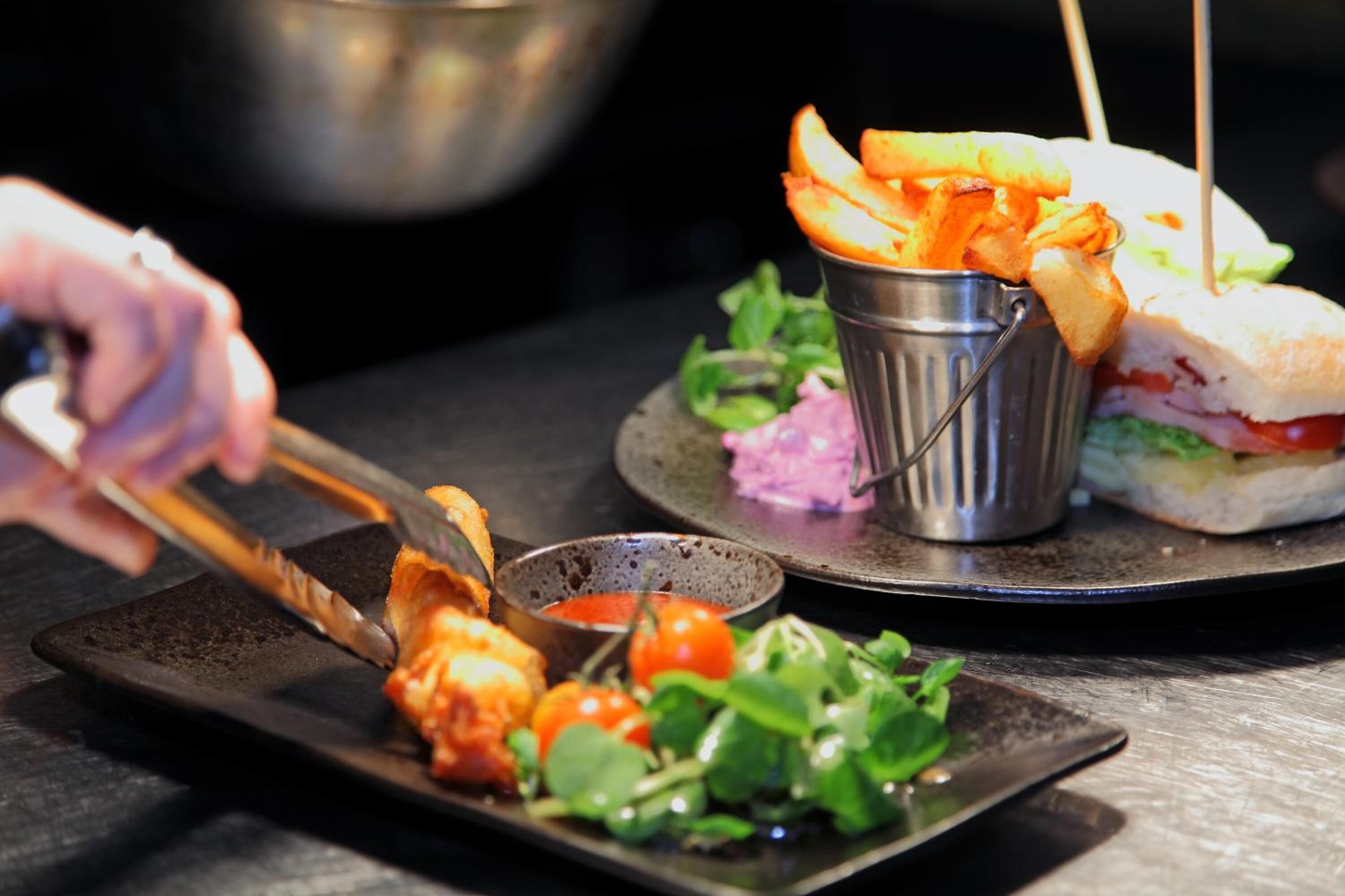 A meal with a sandwich, fries, and a side salad on a black plate.