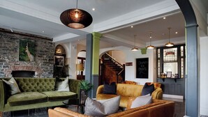 A spacious lobby with a green sofa, a brown leather chair, and a staircase leading to upper floors. - The Hafod Hotel (Aberystwyth)