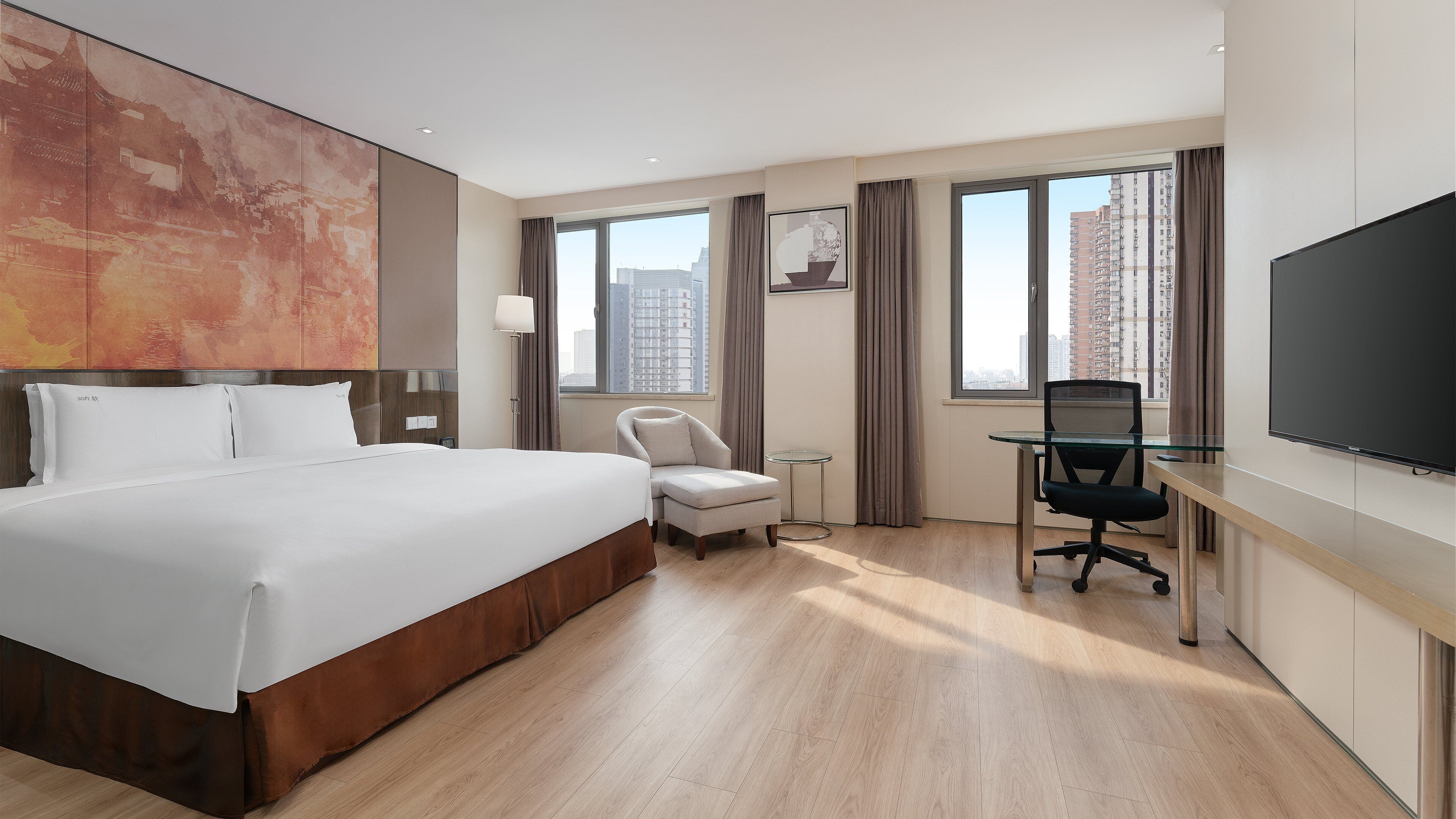 A hotel room with a large bed, a desk with a chair, a TV, and a window with a view of buildings.