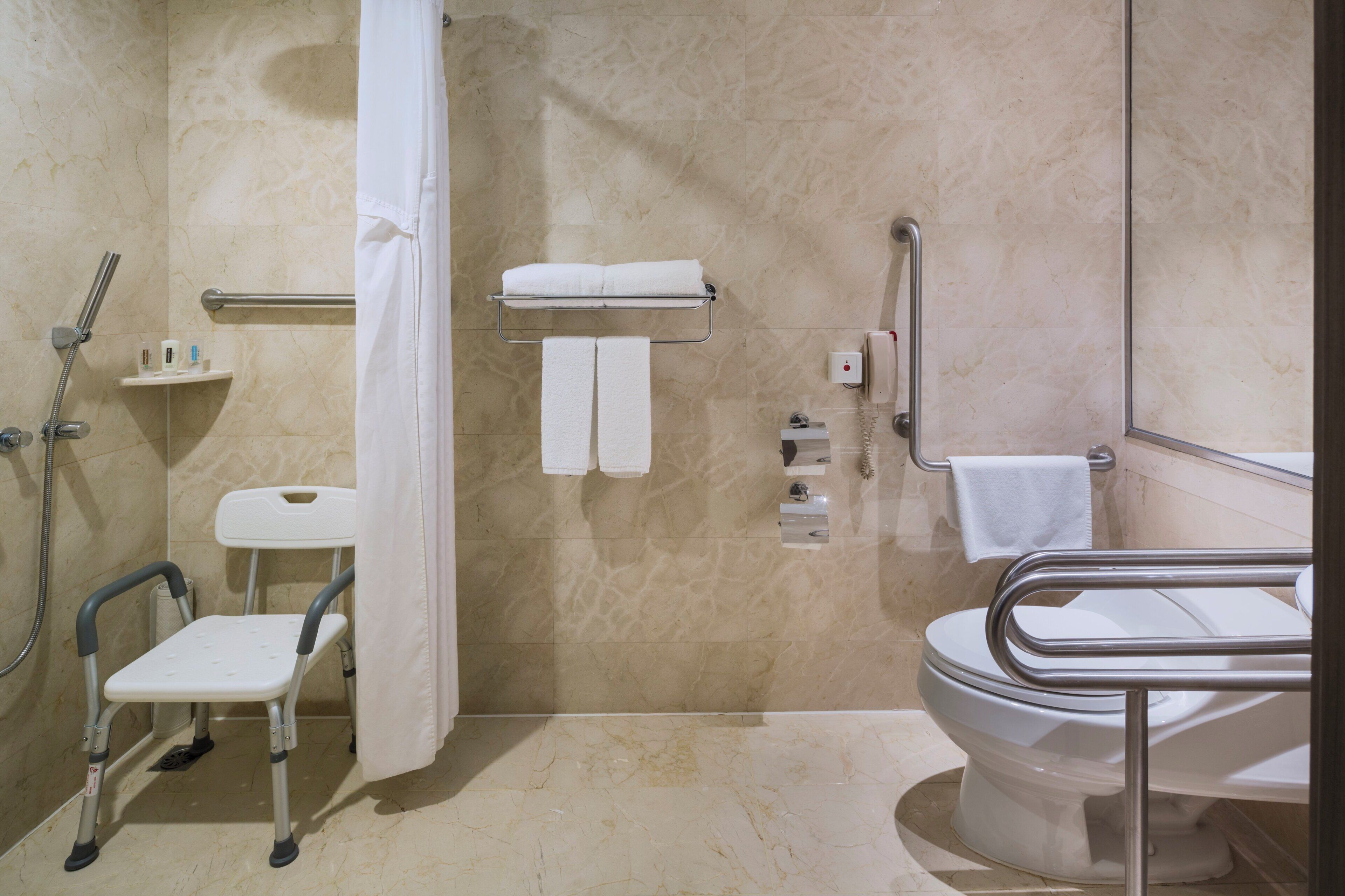 A bathroom with a shower, toilet, grab bars, a step stool, and a towel rack.