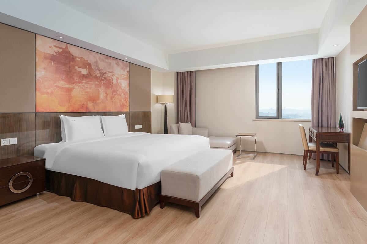 A modern hotel room with a large bed, a desk, and a TV.