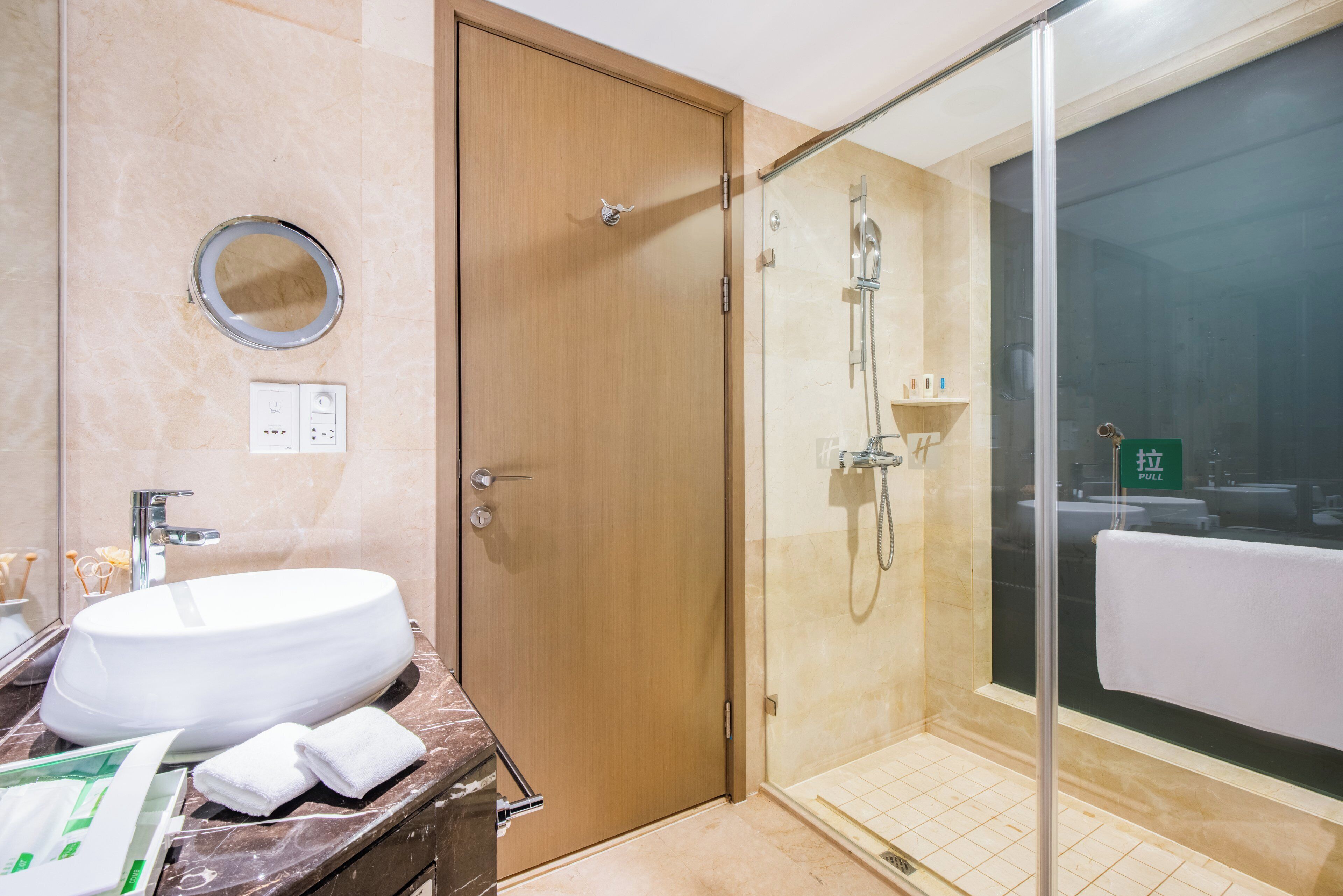 Une salle de bain avec une porte en bois, un lavabo avec un miroir et un espace douche.