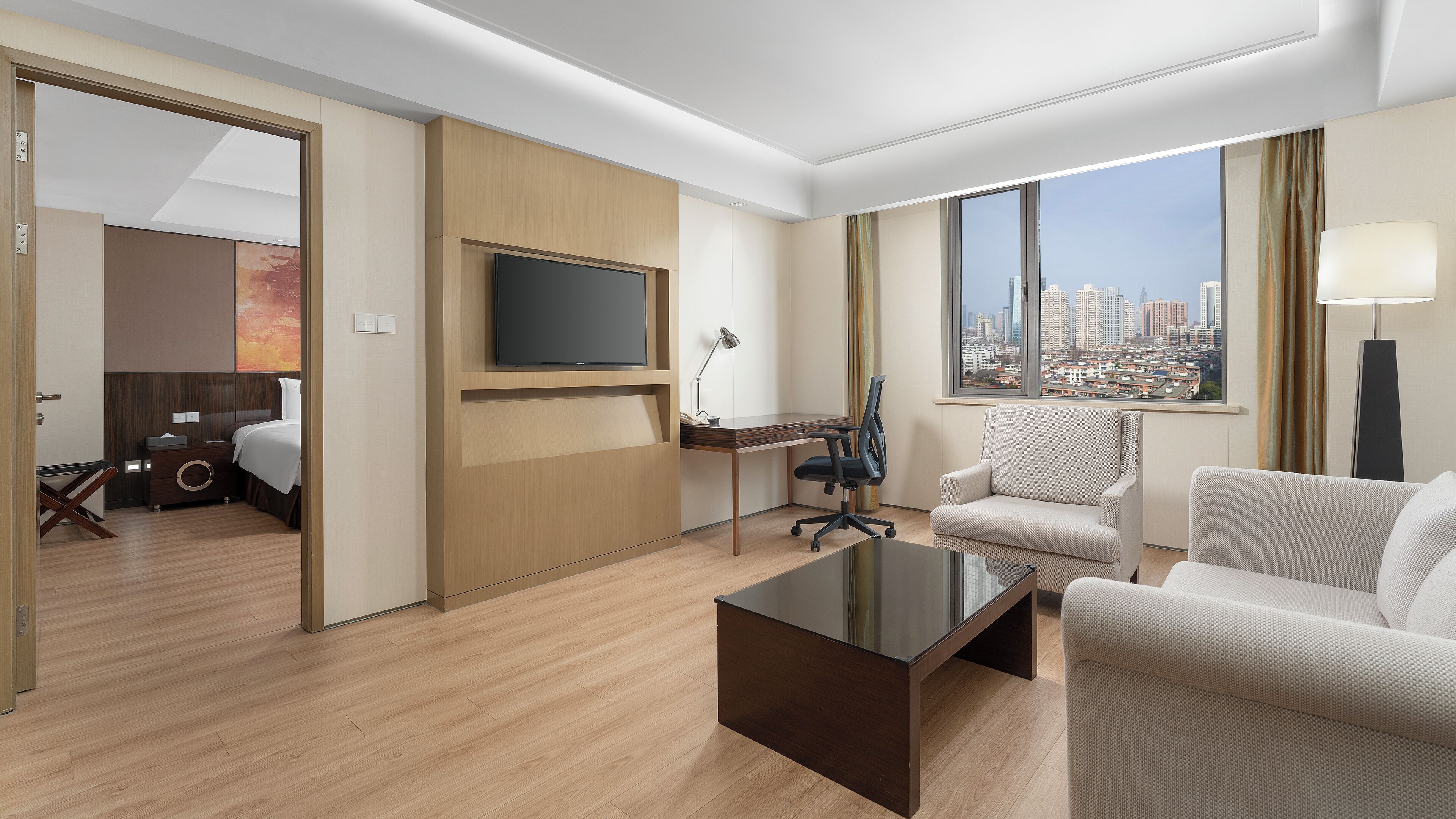A hotel room with a bed, desk, chair, sofa, TV, and a city view.