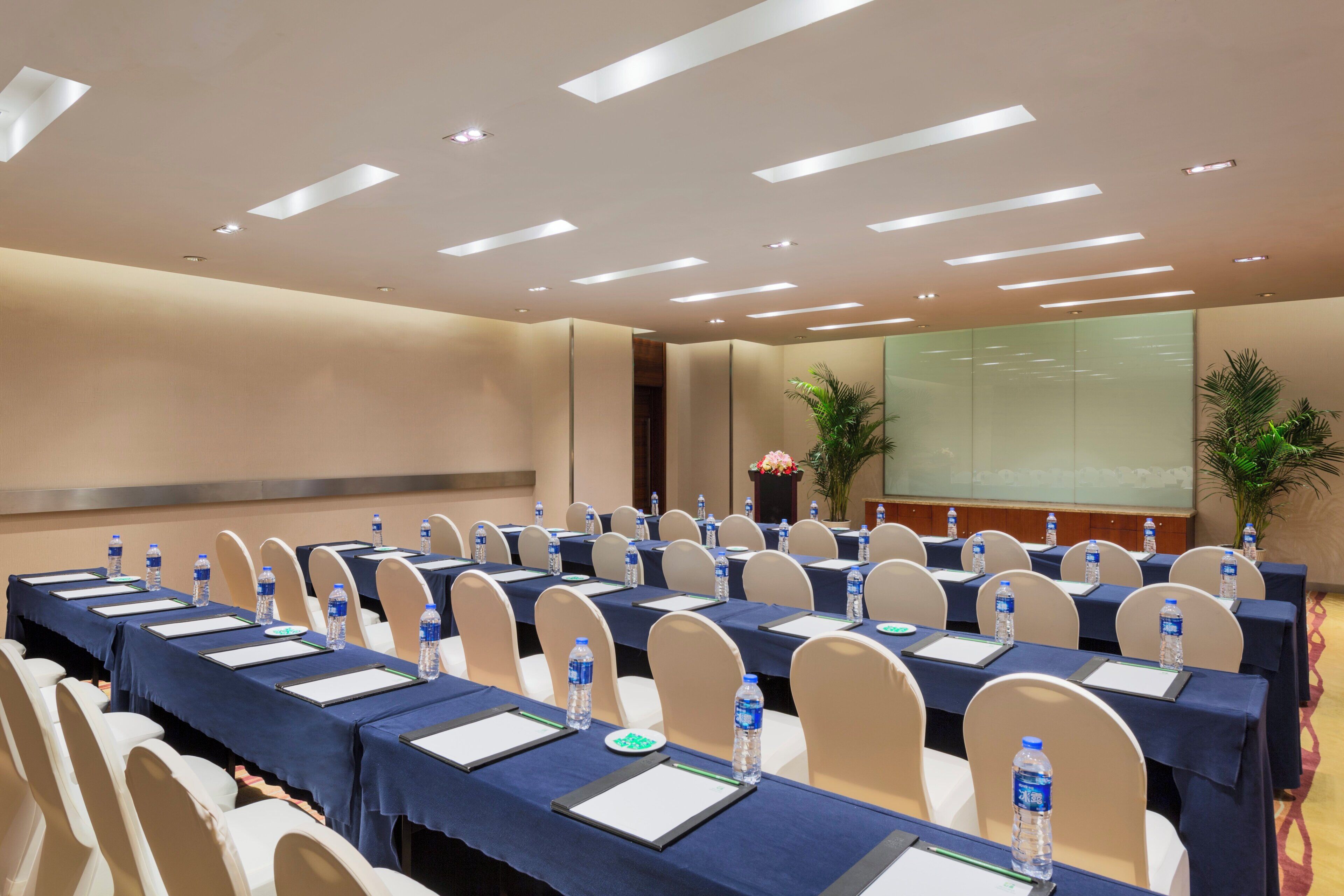 Une salle de conférence équipée de tables, de chaises, de bouteilles d’eau et d’un écran de présentation.