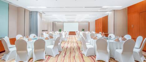 A conference room with rows of tables, white chairs, and a carpeted floor.