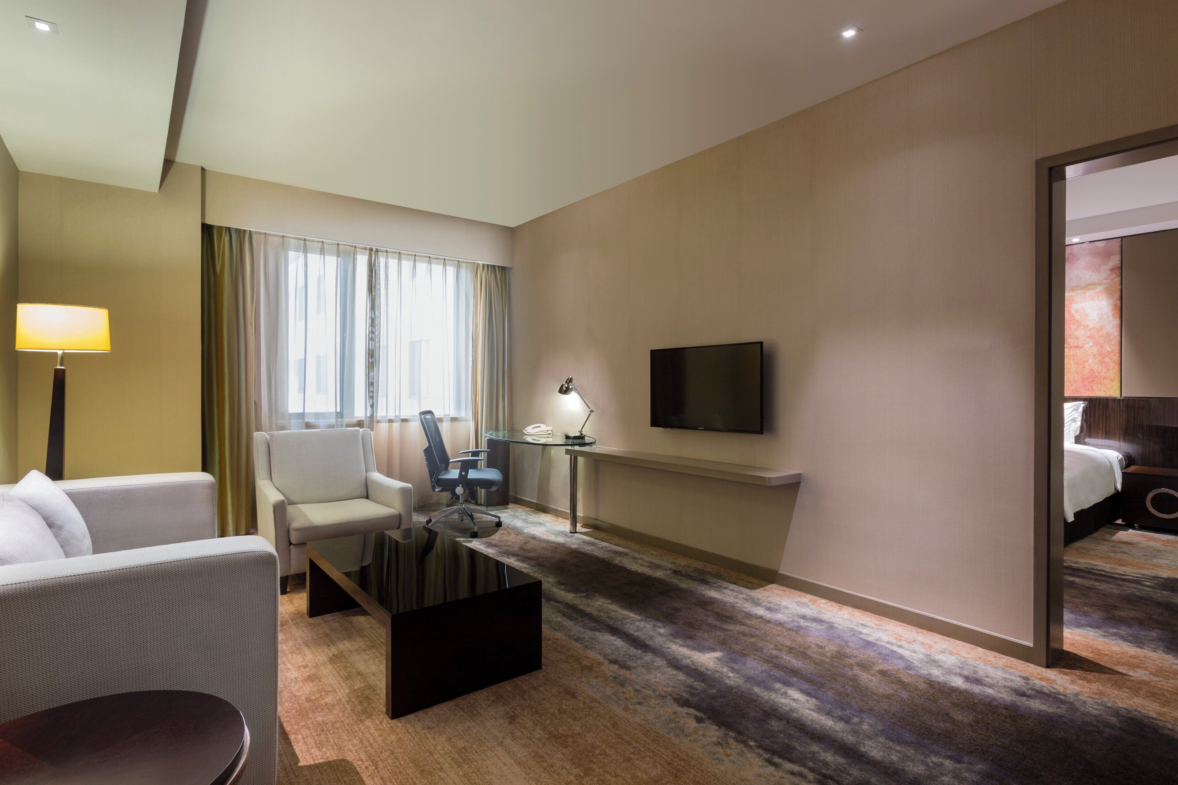 Una habitación de hotel con cama, escritorio, silla, televisor y lámpara.