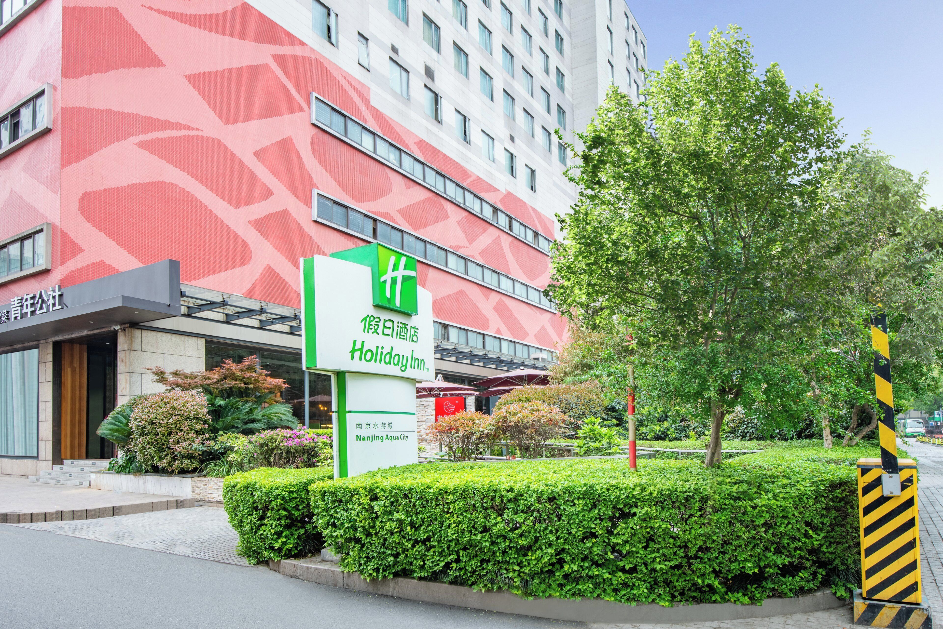 A hotel with a red patterned facade, a green sign for Holiday Inn, and a well-maintained garden area.