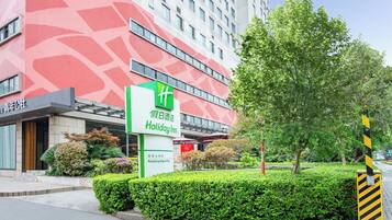 A hotel with a red patterned facade, a green sign for Holiday Inn, and a well-maintained garden area.