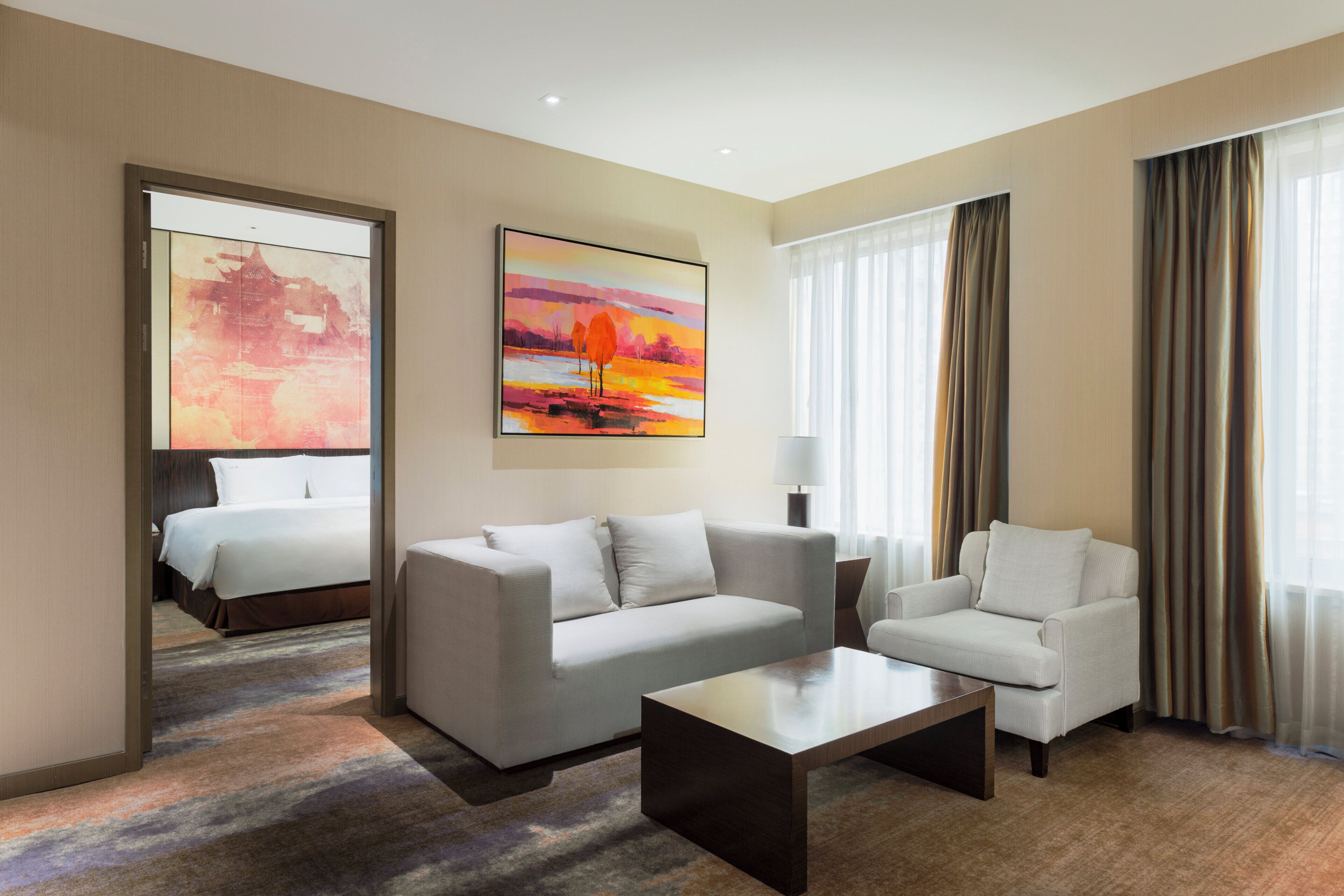 A hotel room with a bed, two sofas, a coffee table, a painting, and a large window with curtains.