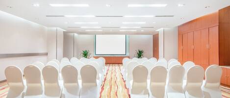 A conference room with rows of white chairs, a projector screen, and a patterned carpet.