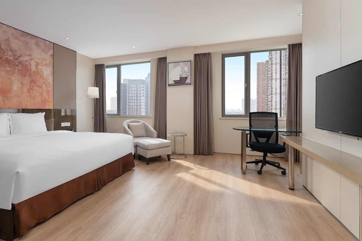 Ein Hotelzimmer mit einem großen Bett, einem Schreibtisch mit Stuhl, einem Fernseher und einem Fenster mit Blick auf Gebäude.