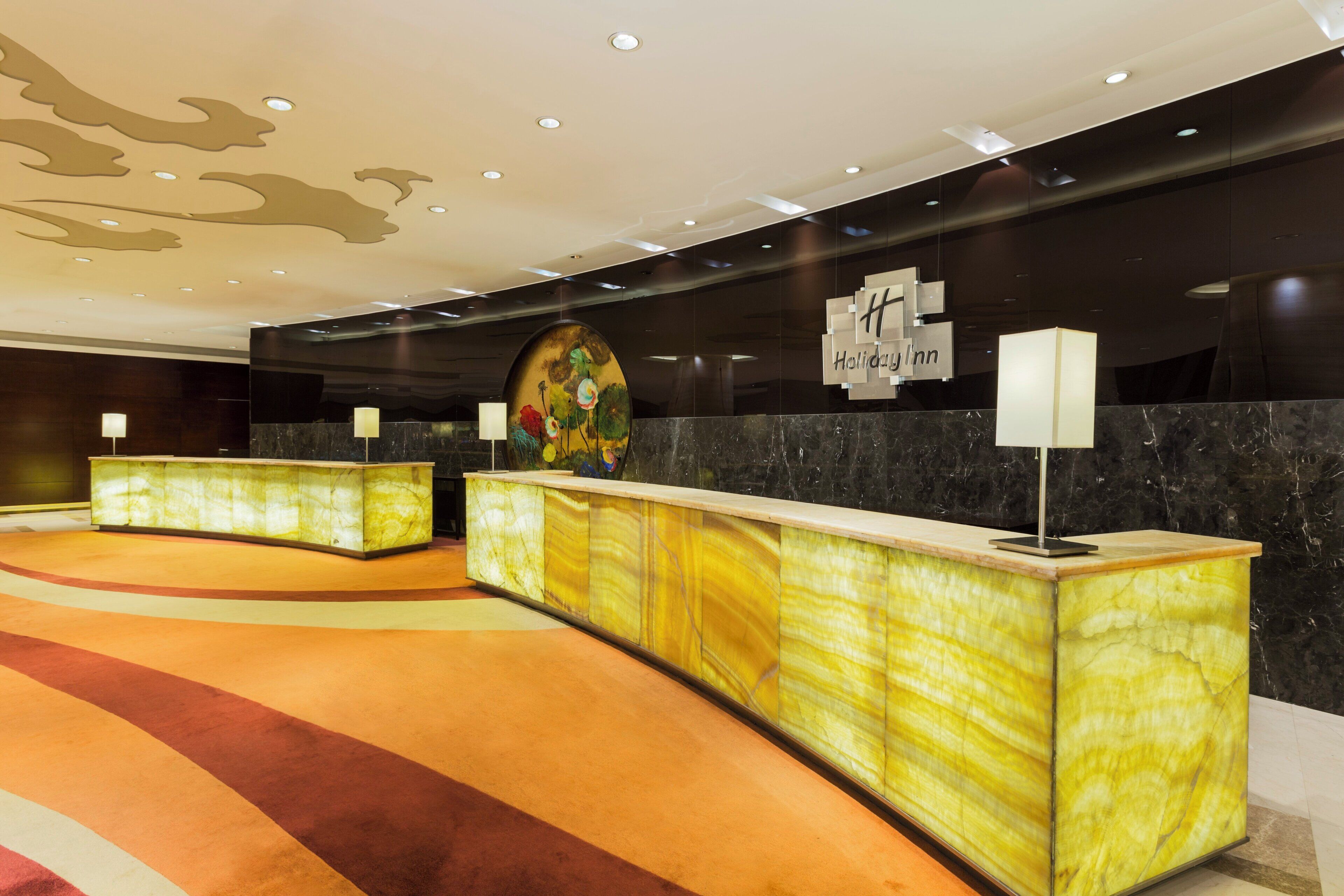 Zona de recepción de un hotel con mostradores de mármol, una gran obra de arte floral y un cartel que dice 'Holiday Inn'.