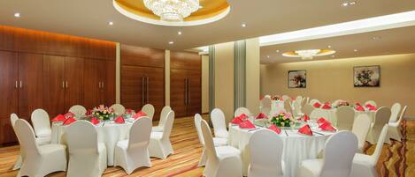 Un salón de banquetes con mesas redondas, sillas blancas y candelabros.