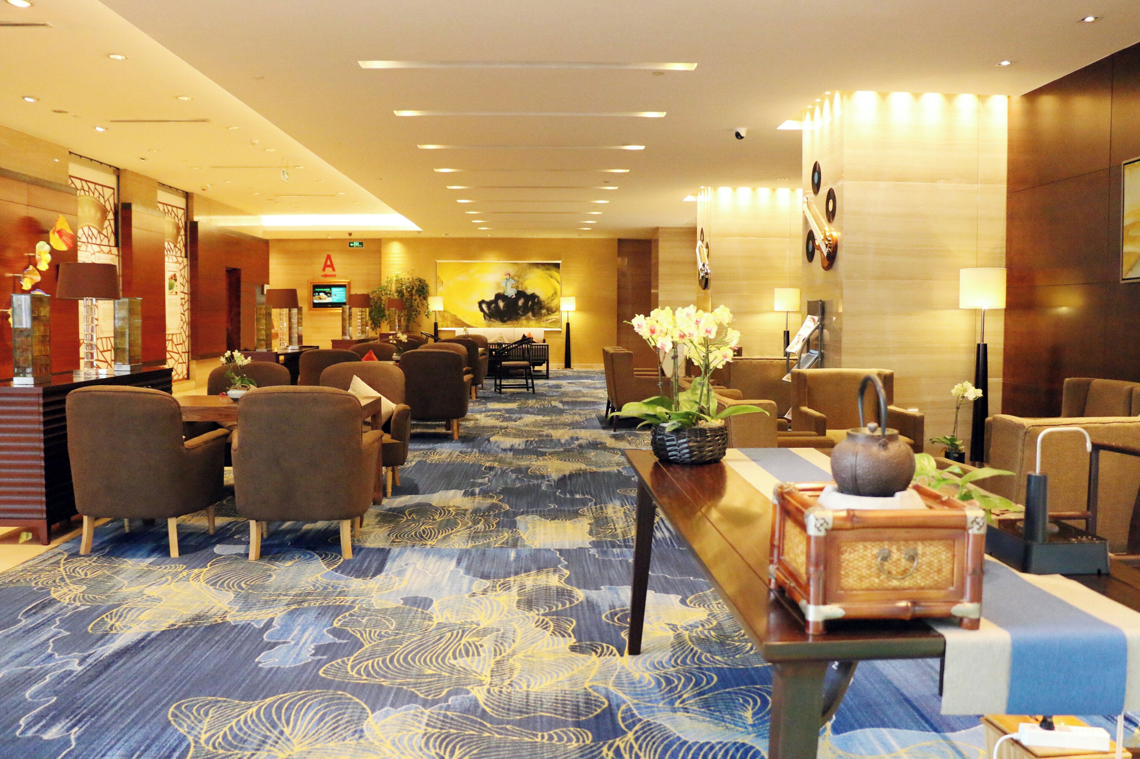A hotel lobby with a reception desk, seating area, and a large wall-mounted television.