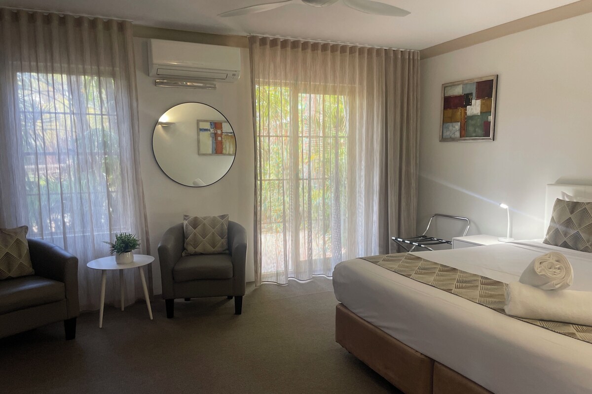 A hotel room with a bed, a chair, a small table, and a ceiling fan.