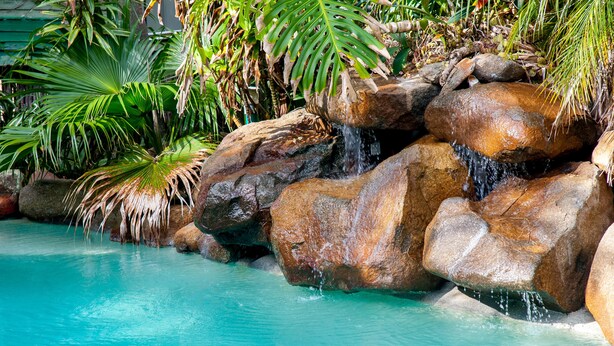 Une piscine aux eaux turquoise et limpides, agrémentée d’une cascade rocheuse, le tout entouré d’une végétation tropicale luxuriante.