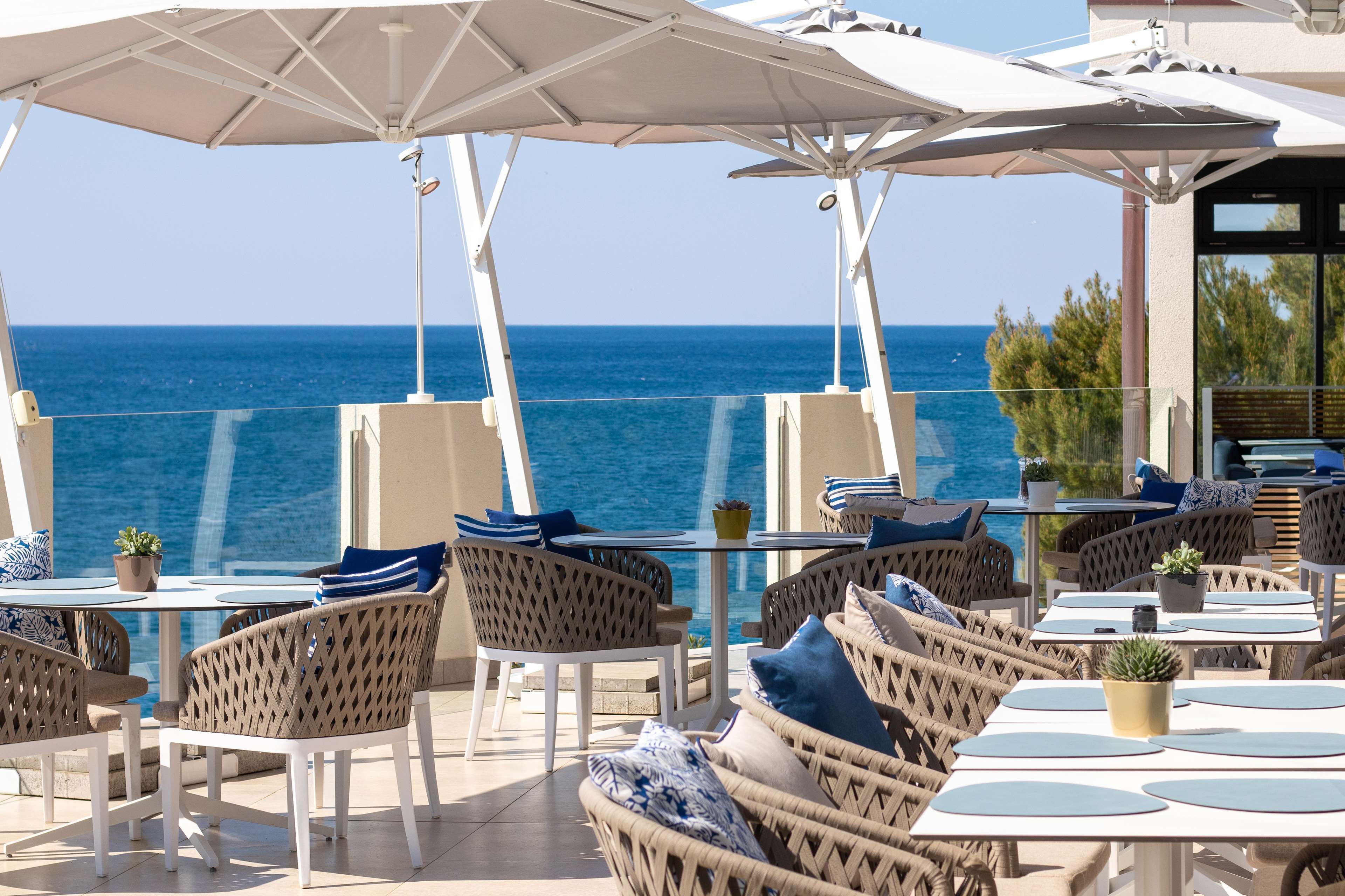 Une terrasse en bord de mer, dotée de meubles en osier, de parasols et offrant une vue sur l’océan.