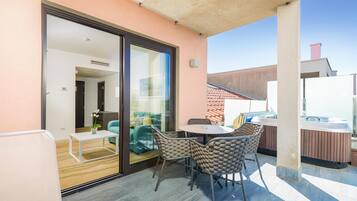 A balcony with a glass door leading to a room, a round table with chairs, and a hot tub.