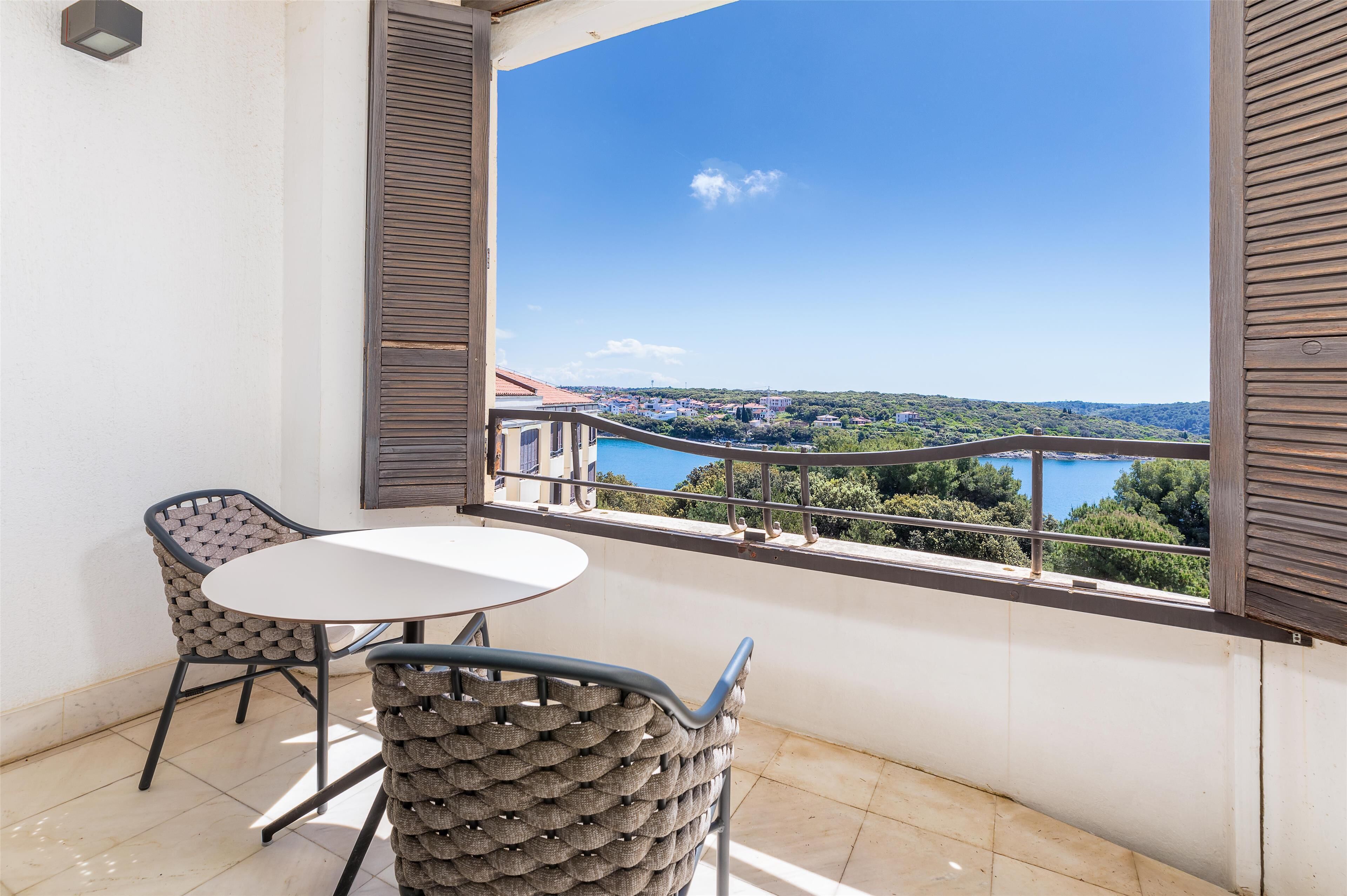 A balcony with a table and two chairs, overlooking a scenic view of a lake and buildings.