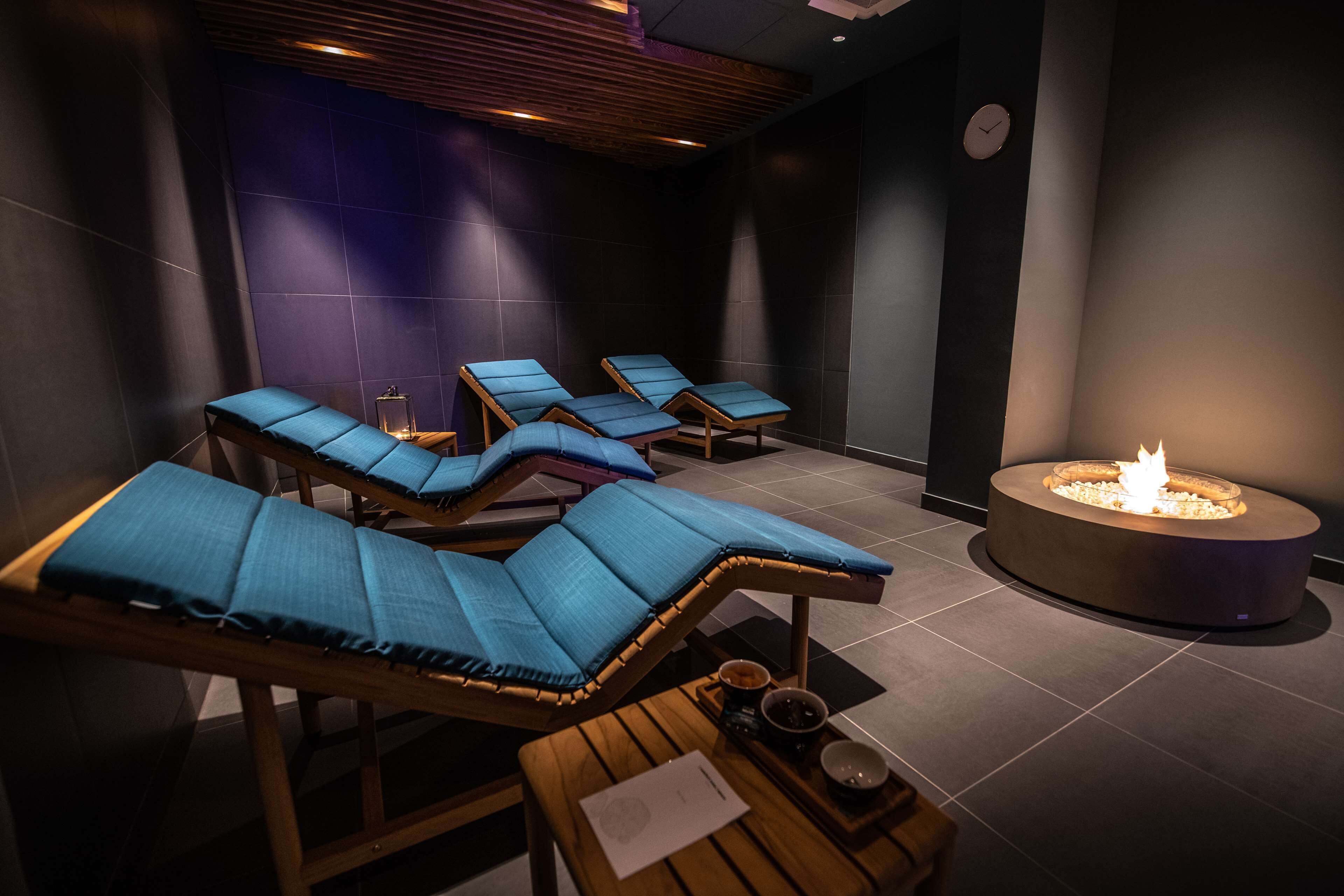 Ein Spa-Raum mit vier Liegestühlen, einem kleinen Tisch mit einer Kerze und einem Kamin.