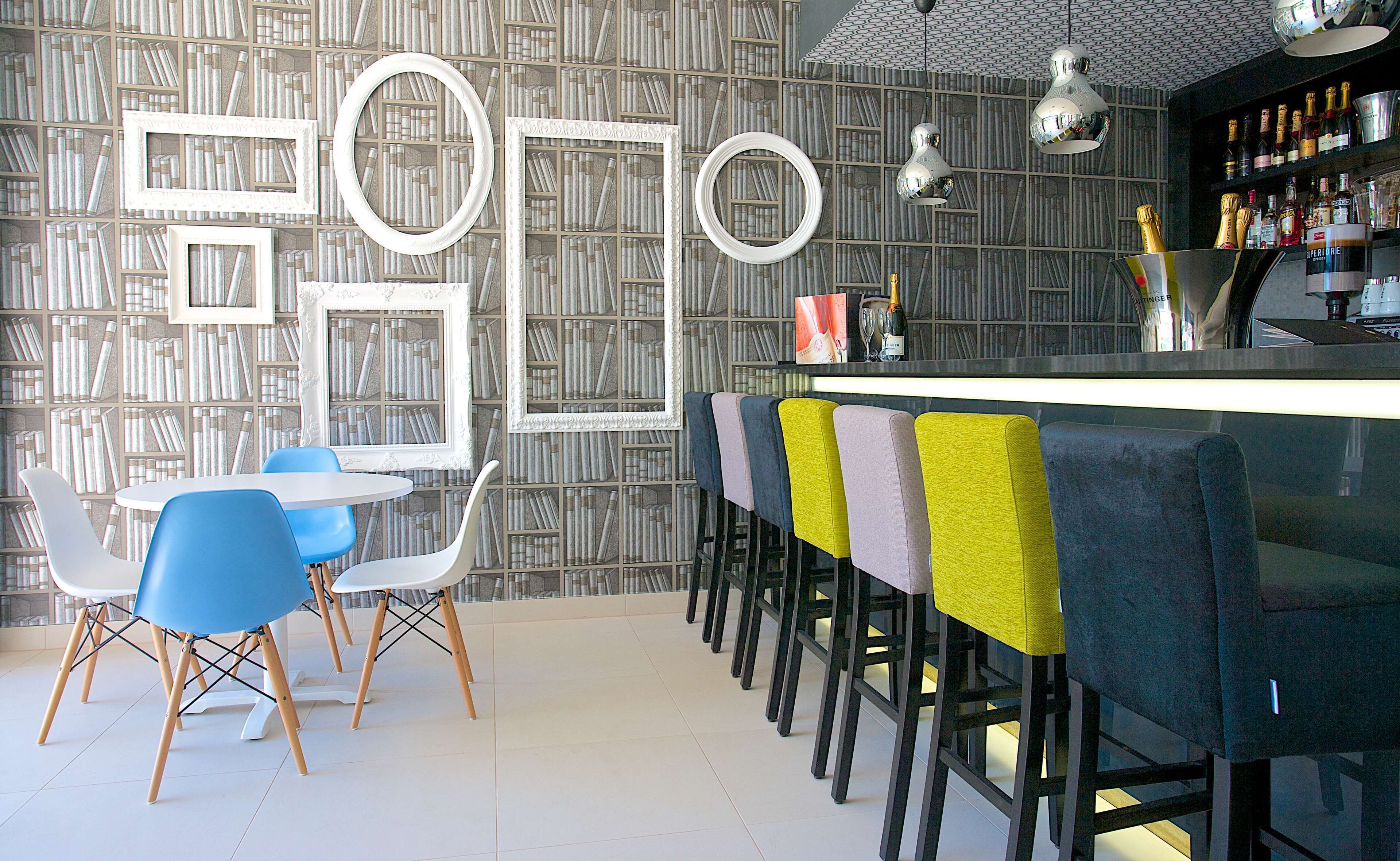 A bar area with a modern design, featuring a bar counter, multiple stools, and a bookshelf with framed pictures.
