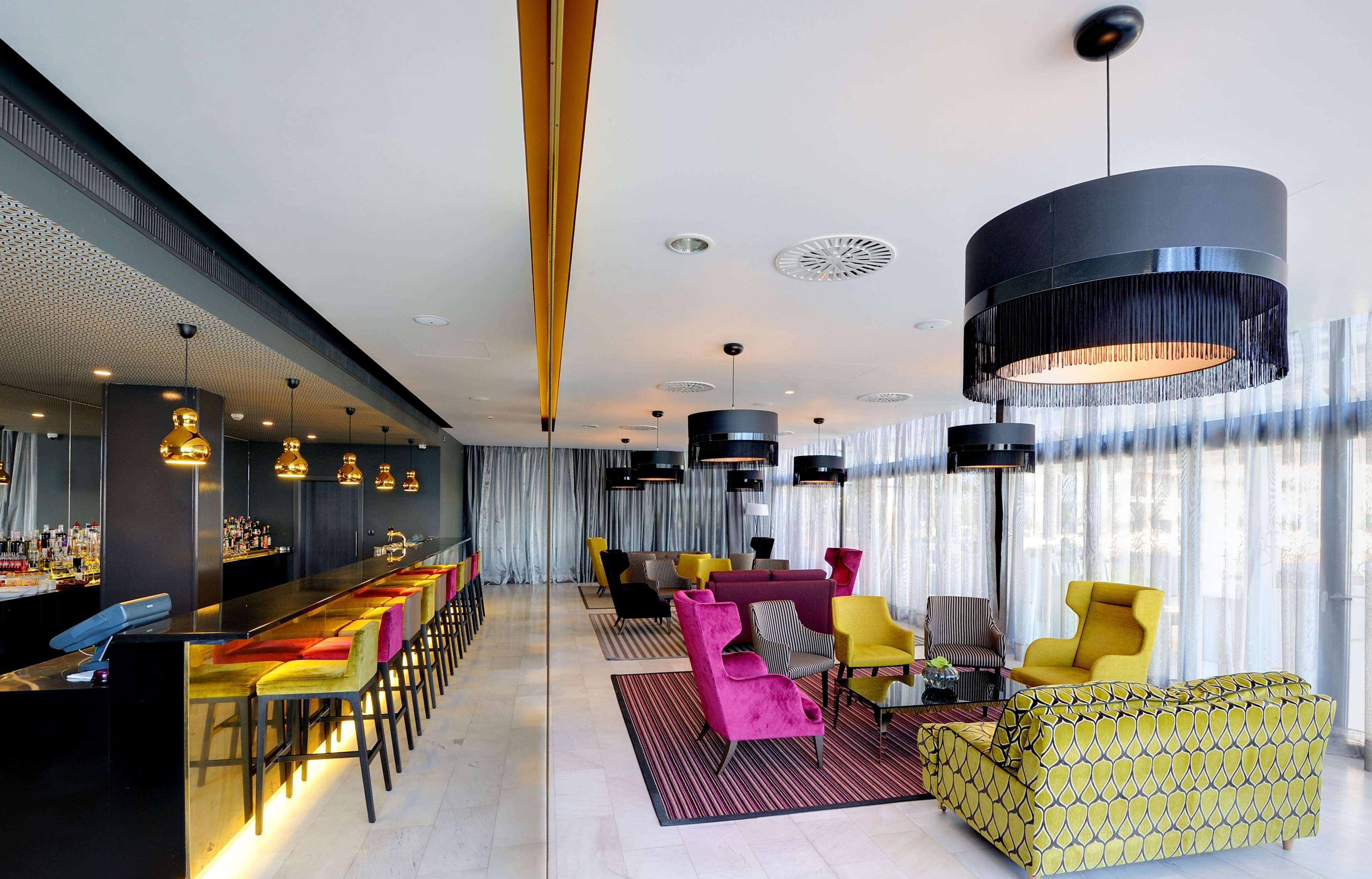A modern bar area with a long counter and multiple seating options, including colorful chairs and sofas.