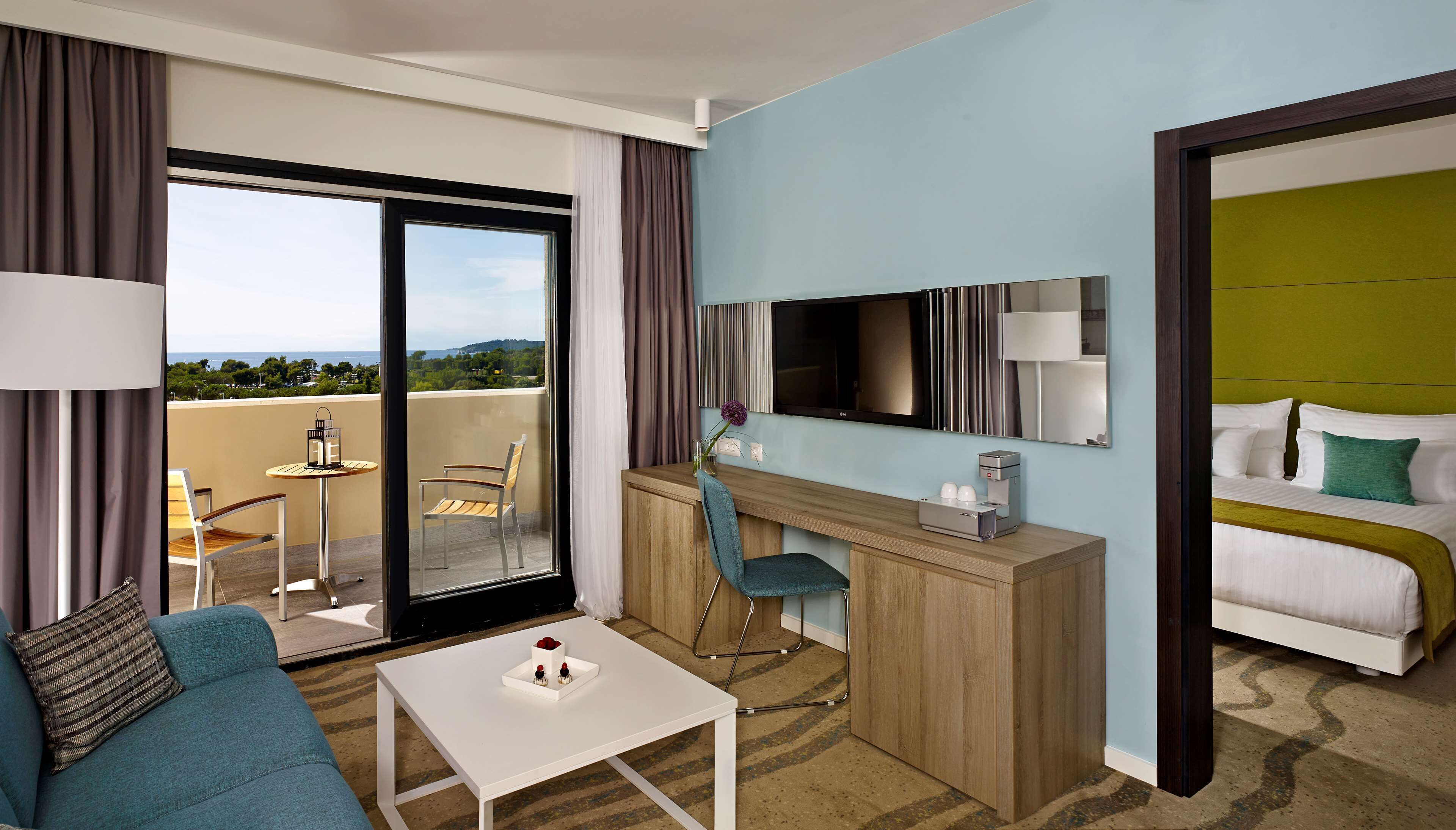 Una camera d'albergo con balcone, una scrivania con sedia, un letto e una televisione.