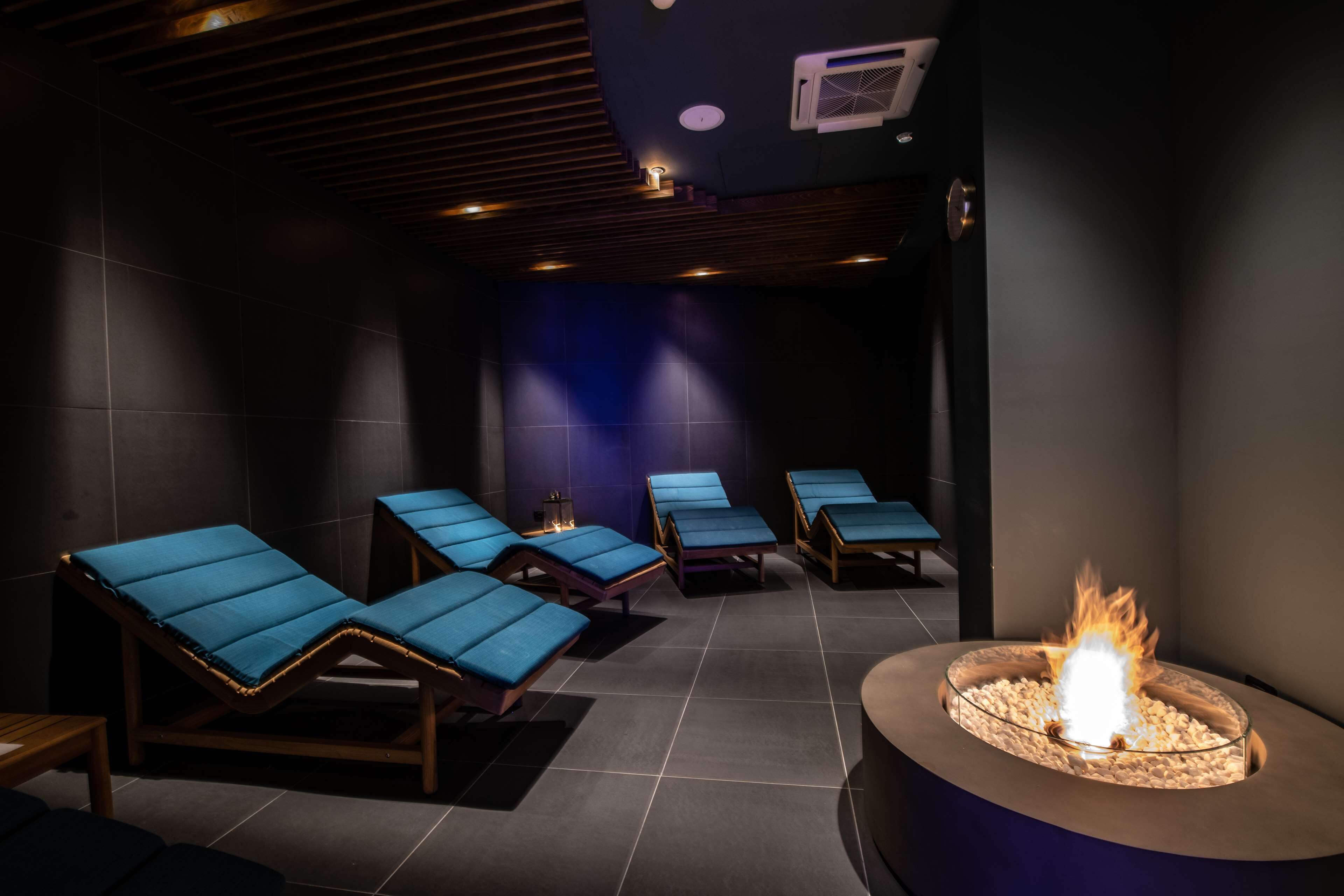 A spa room with four blue lounge chairs arranged around a central fire feature.